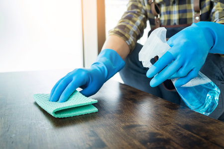 man with cloth cleaning wooden table in home uses rag and fluid in a spray