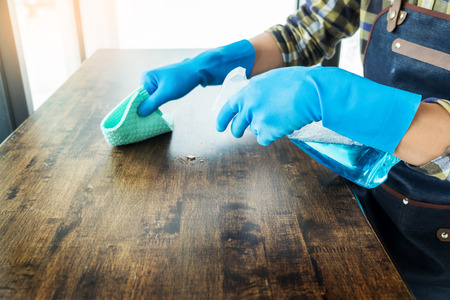 man with cloth cleaning wooden table in home uses rag and fluid in a sprayの写真素材
