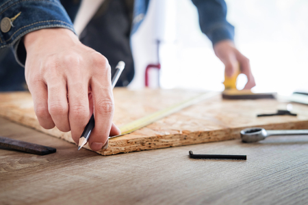 Carpenter working carefully looking at the plans work in carpentry. He is successful entrepreneur at his workplace. hammering a nail Supports On Building Site work with cutterの写真素材