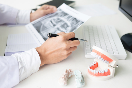 Concentrated dentist sitting at table with jaw samples tooth model in dental office professional dental clinic.の写真素材