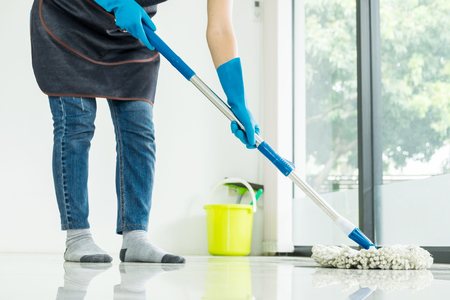 Young housekeeper cleaning floor mobbing holding mop and plastic bucket with brushes, gloves and detergents in the leaving room house floor helping his wifeの写真素材