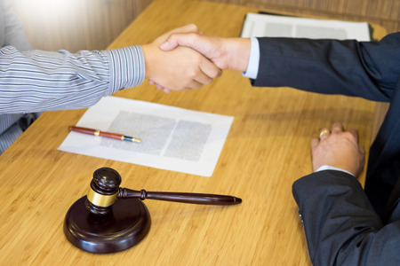 Gavel Justice hammer on wooden table with judge and client shaking hands after adviced in background at courtroom, lawyer service conceptの写真素材