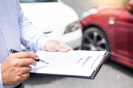 Insurance agent writing on clipboard while examining car after accident claim being assessed and processedの写真素材
