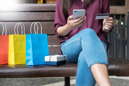 Portrait of a happy shopper paying online with credit card through smartphone with bags in a mallの写真素材