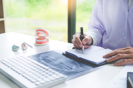 Concentrated dentist sitting at table with jaw samples tooth model in dental office professional dental clinic.の写真素材