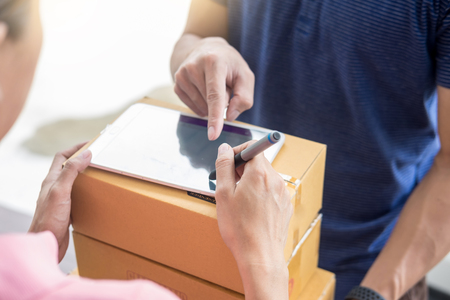 woman courier holding a parcel Shipping Mail appending signature signing delivery note after receiving package from delivery manの写真素材