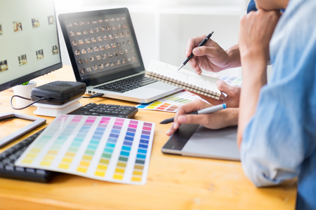 graphic designer team working on web design using color swatches editing artwork using tablet and a stylus At Desks In Busy Creative Officeの写真素材