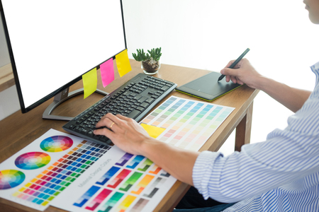 designer Editor at work drawing sketches a new project on graphic tablet and color palette sitting at desk with computer at studio or office.の写真素材