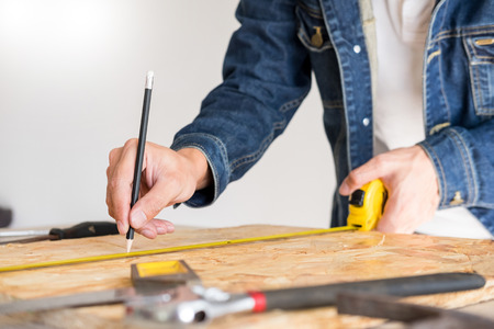 Carpenter working carefully looking at the plans work in carpentry. He is successful entrepreneur at his workplace. hammering a nail Supports On Building Site work with cutterの写真素材