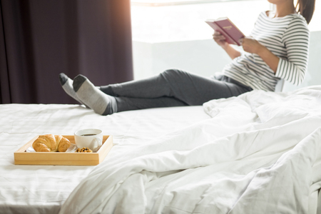 Woman reading book or newspaper and drinking coffee breakfast on bed during the morning.の写真素材