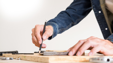Carpenter working carefully looking at the plans work in carpentry. He is successful entrepreneur at his workplace. hammering a nail Supports On Building Site work with cutterの写真素材