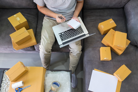 Startup small business SME, entrepreneur owner  using smartphone or note book taking receive and checking online purchase shopping order to preparing pack product boxの写真素材