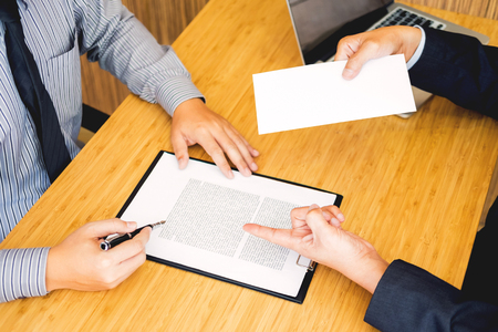 Hand of a businessman hands over a resignation letter final remuneration to executive boss on a wooden table to his boss Change of job, unemployment concept.の写真素材