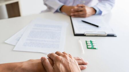 patient listening intently to a male doctor explaining patient symptoms or asking a question as they discuss paperwork together in a consultationの写真素材
