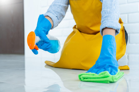 Housekeeper maid wearing rubber gloves with cloth cleaning or applying floor care and cleaners at...