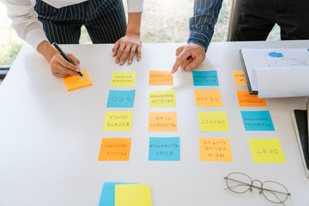Business people arranging sticky notes commenting and brainstorming on work priorities colleague in...