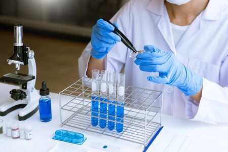 scientists researching in laboratory in white lab coat, gloves analysing, looking at test tubes sample, biotechnology concept.の写真素材