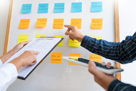 Business people arranging sticky notes commenting and brainstorming on work priorities colleague in...