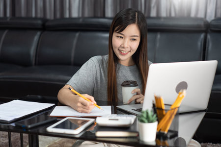 Attractive young beautiful asian woman working with laptop and document drinking coffee at the...