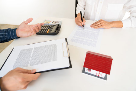 Attractive young beautiful asian woman working with laptop and document talking smartphone at the indoors living room office as a freelancer, e-coaching working, remotely or work from home conceptの写真素材