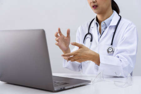 Asian women doctor using her laptop video call to explain medical consultation talking online with patient on webcam virtual conference from hospital,  professional consultation telemedicine conceptの写真素材