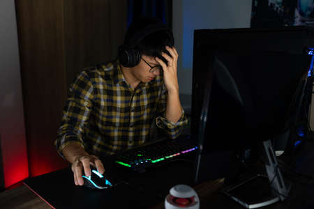 Asian man gamer in headphones stressed with hand feel depressed or angry shocked when losing the video game on computer Fear and upset for mistake, video game technology and e-sport concept.の写真素材