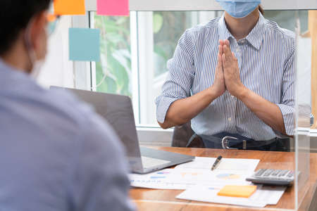 Asian business team colleagues wearing mask greeting by looking through the plastic protective wall, concept of social distancing to prevent the spread of coronaviru COVID-19の写真素材
