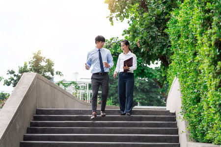 Two asian business coworkers outside office buildings discuss and commenting work to each other.