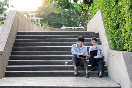 Two asian business coworkers outside office buildings discuss and commenting work to each other.の写真素材