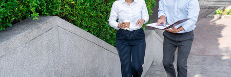 Two asian business coworkers outside office buildings discuss and commenting work to each other.