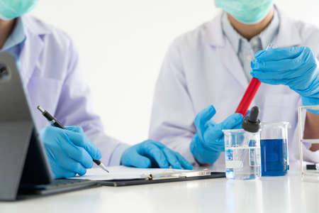 Attractive young scientist team in lab coat and safety goggles working with analysing test trial or investigations with test tubes in laboratoryの写真素材