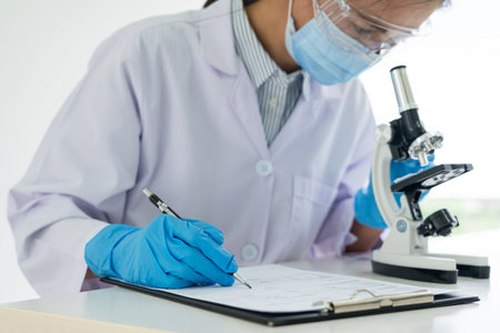 Young Asian scientist Working looking through a microscope doing research for analyzing a...