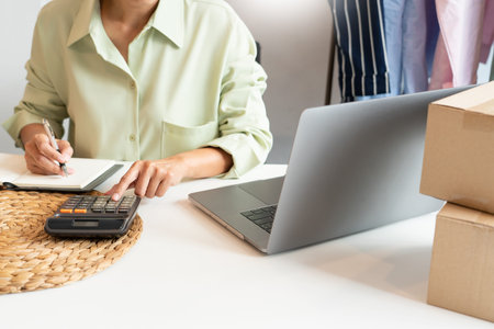 Asian business owner working at home with packing box of her online store prepare to deliver...