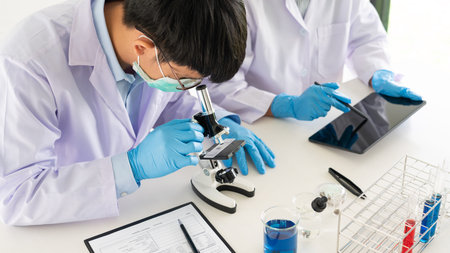 Attractive young scientist team in lab coat and safety goggles working with analysing test trial or...