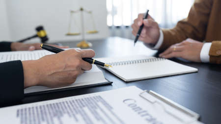 law,libra scale and hammer on the table, 2 lawyers are discussing about contract paper, law matters determination, showing paper and notes.の写真素材