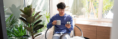 Handsome Asian teenager man wearing casual clothes in glasses using smart phone browsing Internet on...