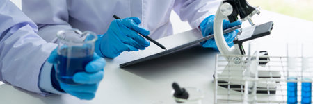 Attractive young scientist team in lab coat and safety goggles working with analysing test trial or...