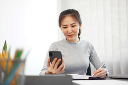 Office work concept a female officer using a mobile phone to check meeting agenda for tomorrow.の写真素材