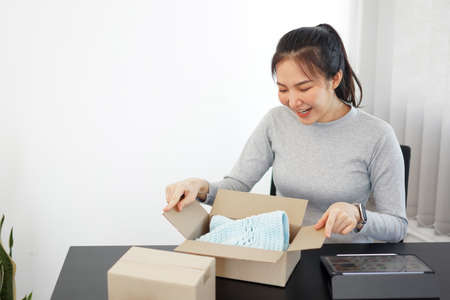 Shopping online concept a smiling woman unboxing an arriving parcel to check the products she bought after waiting with an effort.の写真素材