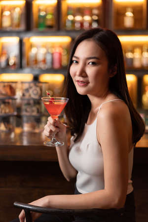 Nightlife concept a sexy young woman with long hair holding the pink champaign sitting enjoying the fun atmosphere in the bar.の写真素材