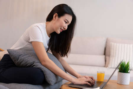 Living room concept in the coffee shop a girl with a bun hair using her laptop going on the internet with a glass of orange juice.の写真素材