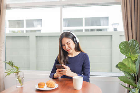 Work from home concept a young woman wearing headphone enjoying a moment listening to her favorite playlist with desserts and a drink on the table.の写真素材