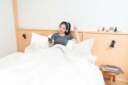 Bedroom concept on the comfortable bed a girl listening her favorite songs by wearing a headphone in the morning.の写真素材