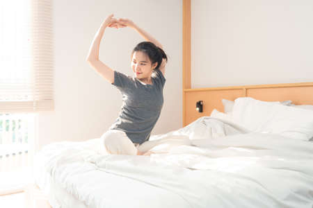 Bedroom concept in the morning the pretty girl just waking up and stretching her body on the brown wooden bed.の写真素材