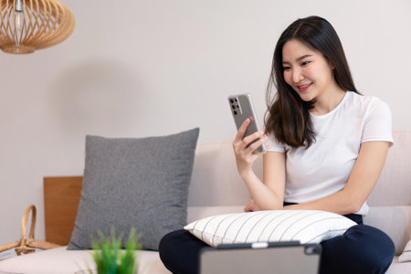 Living room concept a pretty girl sitting on the comfortable sofa spending her leisure on online with juice and snacks in the living room.の写真素材