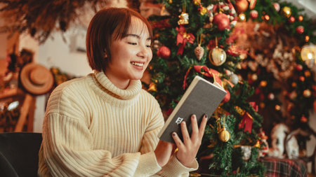 a young Woman in front of Christmas tree reading a book at home with x-mas decorationの写真素材