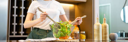 salad concept the woman with white t-shirt and dark green pants standing at the kitchen and making a bowl of green salad.の写真素材