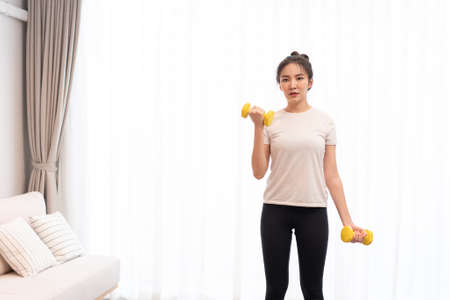 Productive activity concept a girl with a bun wearing a white t-shirt raising the yellow dumbbell with her right hand in her living space.の写真素材