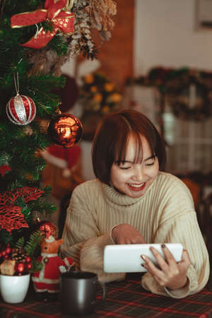 Young smiling woman looking on a tablet with christmas tree in background.の写真素材