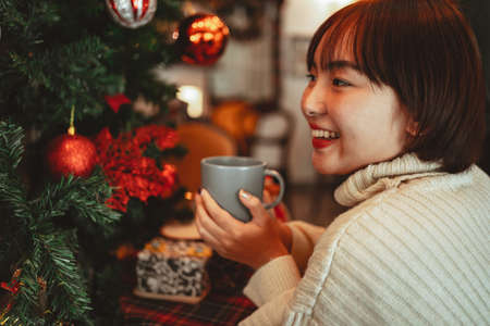 Happy women holds a cup of coffee and smell aromatic near a Christmas tree decoration.の写真素材